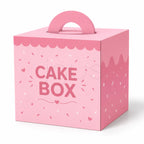A pink cardboard cake box with a built-in handle, decorated with scalloped frosting-style edges, sprinkle details, and the words 'CAKE BOX' on the front, shown on a white background.