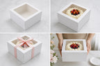 White cake box with a cake inside, decorated with berries and a pink ribbon.