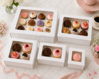 Assorted cupcakes in different size white cupcake boxes on a decorative table with flowers and ribbons.