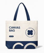 A canvas tote bag with dark navy blue handles and a navy blue bottom panel, featuring printed text and a four-leaf clover graphic on an off-white body, shown on a clean white background.